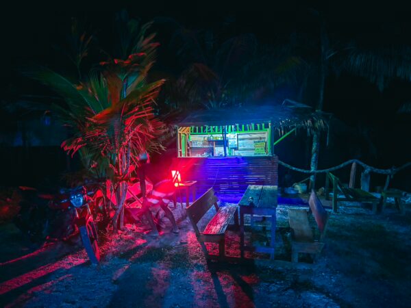 Colorful lights illuminate a vibrant stall surrounded by tropical plants and benches at night in Ladrilleros, Valle del Cauca, Colombia.
