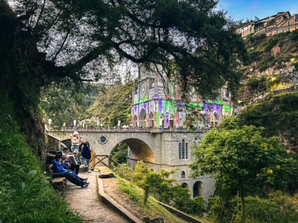 Visitors relax on a path beside the stunning Las Lajas Sanctuary, nestled in a lush valley in Narino, Colombia.