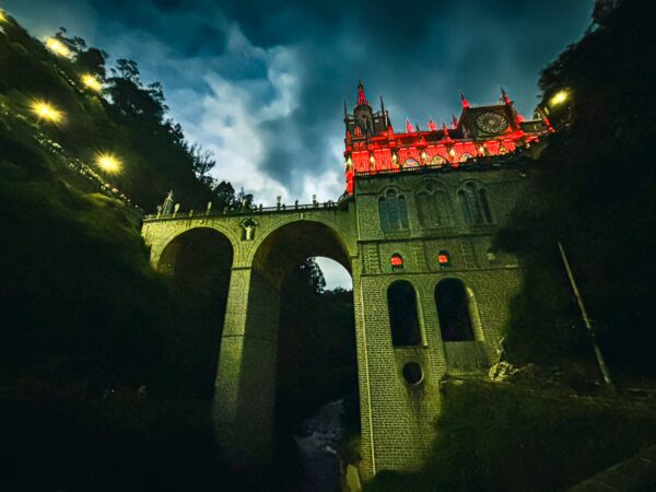Stunning view of the Las Lajas Sanctuary illuminated in red, set against a dramatic sky in Nariño, Colombia.
