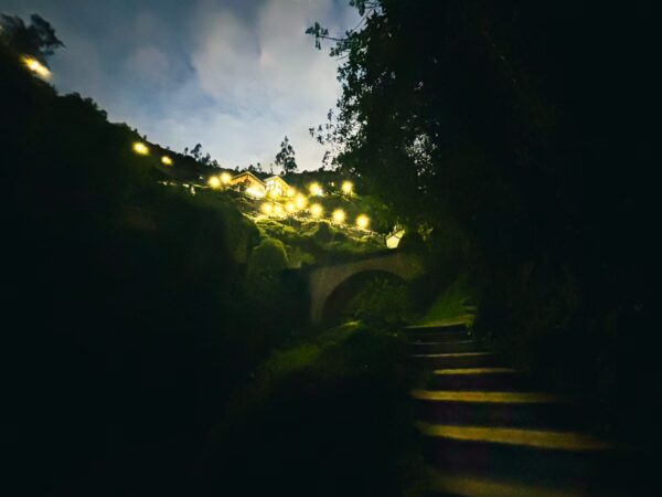 Twinkling lights illuminate a winding pathway leading to a stone bridge in Las Lajas, Nariño, Colombia.