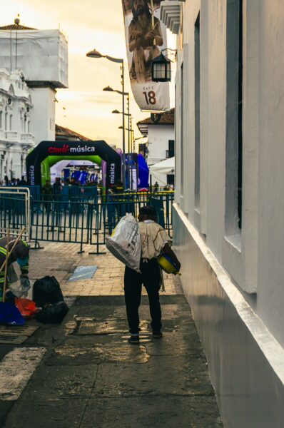 A person walks along the cobblestone street of Popayán, carrying items, with colorful festival decorations in the background.