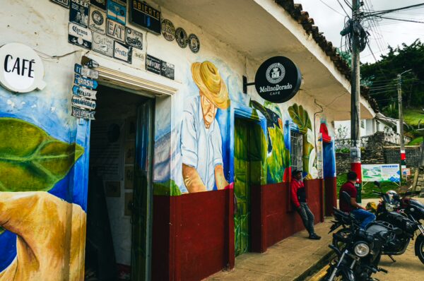Colorful murals depicting local culture adorn the exterior of Molino Dorado Cafe in Silva, Cauca, Colombia, surrounded by motorcycles.