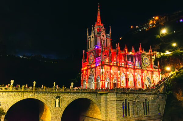 Las Lajas Sanctuary illuminated at night, showcasing its intricate architecture and vibrant colors over the bridge in Nariño, Colombia.
