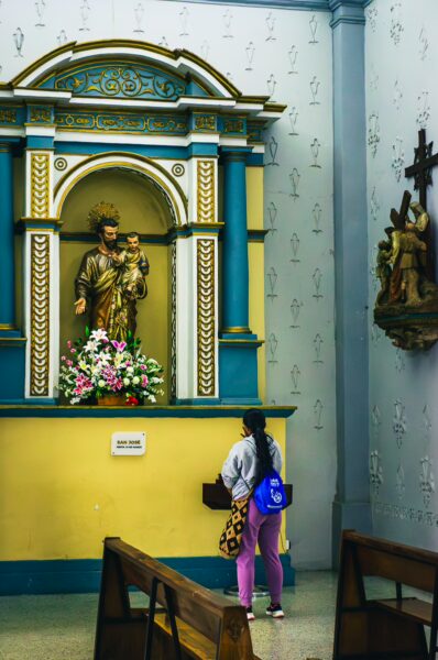 Assumption Cathedral features a colorful altar with a statue surrounded by flowers and a visitor admiring the intricate details in Popayán, Cauca.