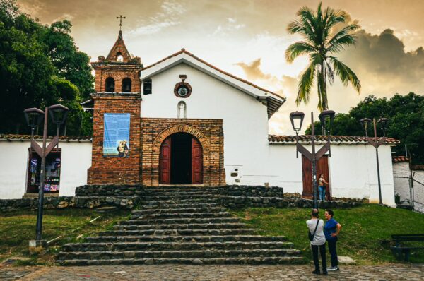 Charming colonial architecture at Colina de San Antonio, Cali, with lush greenery and a vibrant sunset sky.