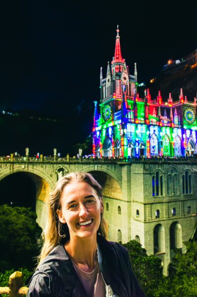 Illuminated Las Lajas Sanctuary shines in vibrant colors at night, featuring a smiling visitor in the foreground, Narino, Colombia.