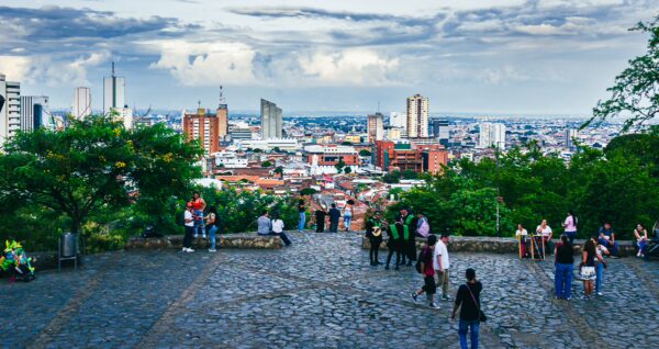 Overview of Cali's skyline from Colina de San Antonio, showcasing vibrant city life and lush greenery against a cloudy sky.