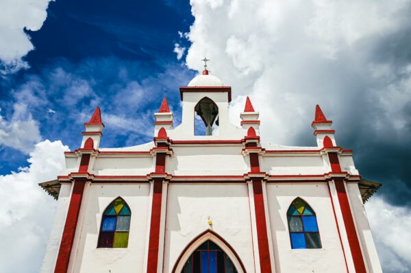 Brightly colored church with red accents and stained glass windows under a dramatic sky at Belen Hill, Silva, Cauca, Colombia.