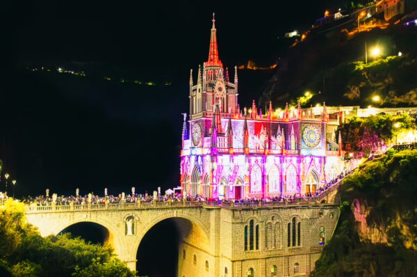 Las Lajas Sanctuary illuminated at night, showcasing vibrant lights against the dark landscape in Narino, Colombia.