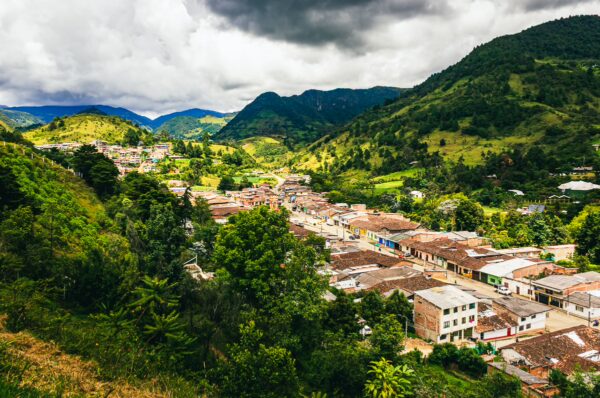 Lush green hills and a colorful village landscape under a cloudy sky at Belen Hill, Silva, Cauca, Colombia.