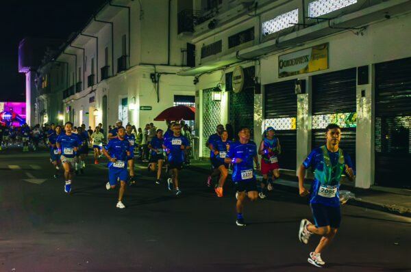 Runners in vibrant blue shirts pass historic buildings during a nighttime marathon in Popayán, Cauca, Colombia.