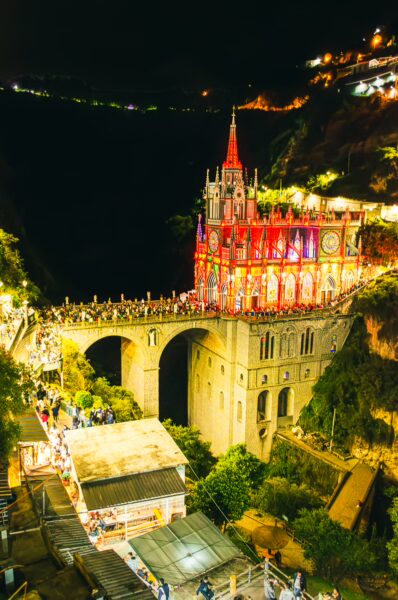 Stunning Las Lajas Sanctuary illuminated at night, perched on a gorge, with vibrant lights and crowds admiring its architecture in Nariño, Colombia.