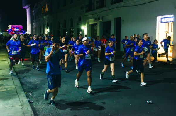Runners in blue shirts participate in a nighttime race along the streets of Popayán, Cauca, Colombia.