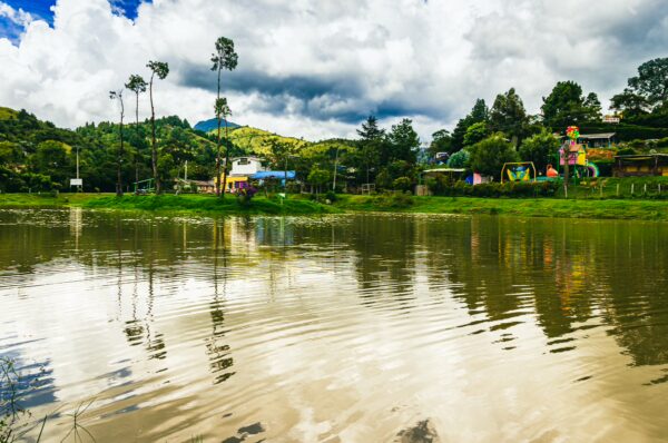 Lago Chiman reflects lush green hills and vibrant homes, with palm trees lining the water's edge in Cauca, Colombia.