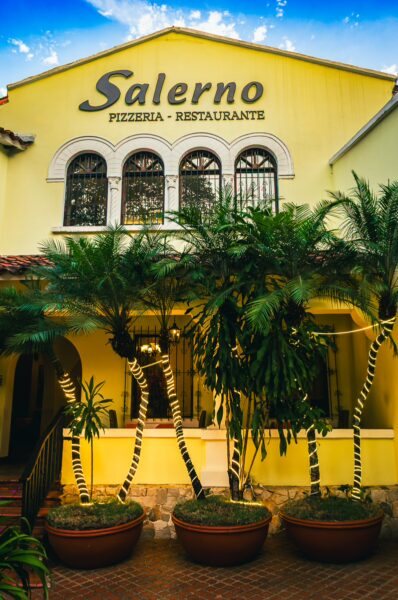 Colorful facade of Salerno Pizzeria, featuring vibrant yellow walls and tropical plants in Cali, Valle del Cauca, Colombia.