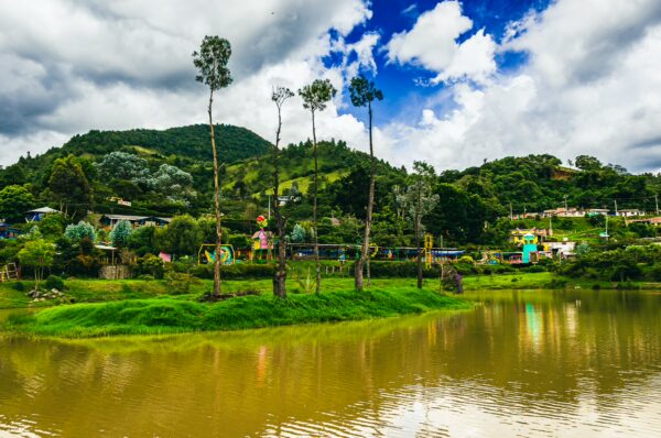 Lago Chiman Silva, with lush greenery and vibrant houses, reflects under a dramatic sky in Cauca, Colombia.