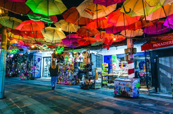 Colorful umbrellas hang over a vibrant street market in Las Lajas, Nariño, Colombia, filled with crafts and local goods.