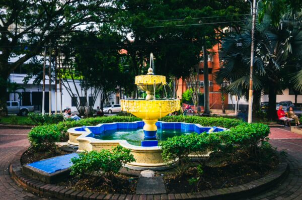 Colorful fountain surrounded by lush greenery and benches in El Peñón, Cali, Valle del Cauca, Colombia.