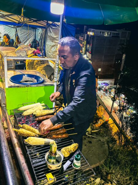 Street vendor grilling corn on skewers at a vibrant night market in Las Lajas, Nariño, Colombia, creating a lively atmosphere.