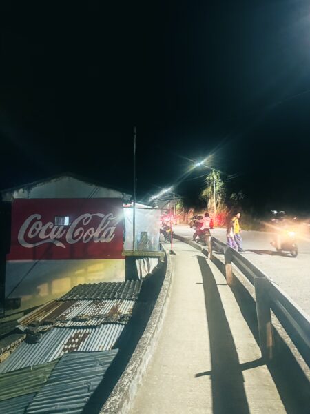Vibrant street scene at night in Las Lajas, Narino, Colombia, featuring illuminated buildings and people along the road.