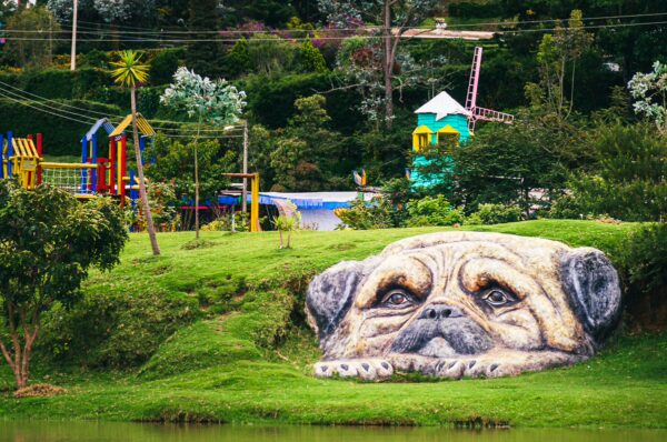 Lago Chiman features a large mural of a pug on a hillside, surrounded by vibrant playground equipment and lush greenery in Cauca, Colombia.