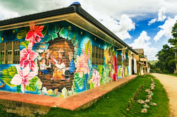 Colorful mural depicting local culture and flowers on a building along a dirt road in Cauca, Colombia. Vibrant street art enhances the scene.