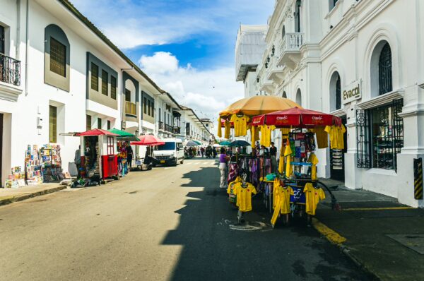 Colorful stalls selling yellow shirts line a charming street in Popayán, Cauca, Colombia, against a backdrop of white colonial buildings.