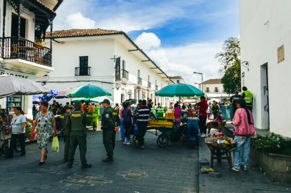 Vibrant street market scene in Popayán, Cauca, with colorful umbrellas, vendors, and local shoppers under a blue sky.