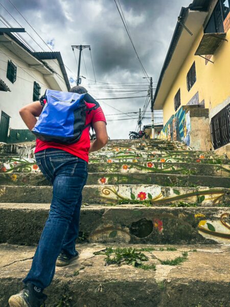 Colorful floral designs adorn the stone steps as a traveler ascends towards the vibrant buildings of Silva, Cauca, Colombia.