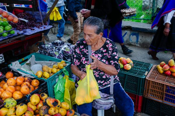 Colorful fruit market scene in Silva, Cauca, Colombia, featuring a woman selecting mangoes among vibrant produce and vendors.