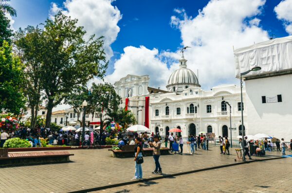 Vibrant scene at Parque Caldas in Popayán, Colombia, showcasing a lively crowd, white colonial architecture, and blue skies.