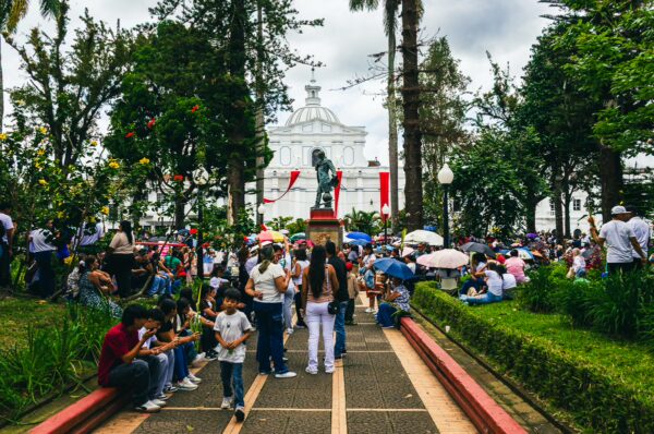 Vibrant Parque Caldas in Popayán, Colombia, bustling with people, green trees, and a statue, set against a cloudy sky.