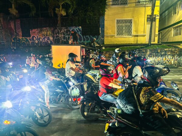 Vibrant night scene in Valle del Cauca, Colombia, showcasing a bustling crowd of motorcyclists and colorful street lights.