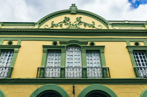 Vibrant yellow colonial building with green trim and ornate balcony details in Popayán, Cauca, Colombia.