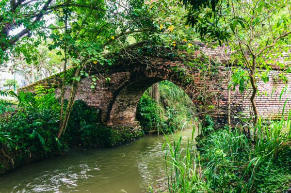 Puente del Humilladero arches over a tranquil stream, surrounded by lush greenery in Popayán, Cauca, Colombia.