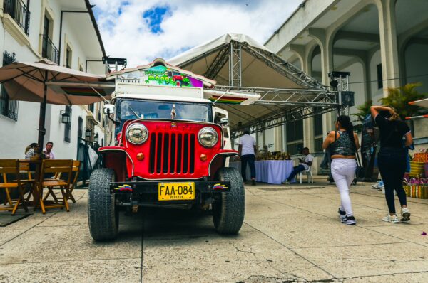 Colorful jeep parked on a cobblestone street, visitors strolling by, with historic architecture in the background in Popayán, Cauca, Colombia.
