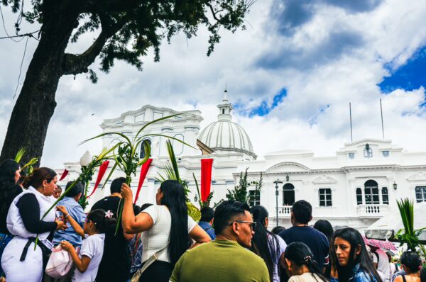 Crowd gathered near white colonial buildings and a dome at Parque Caldas in Popayán, Cauca, Colombia, under a cloudy sky.