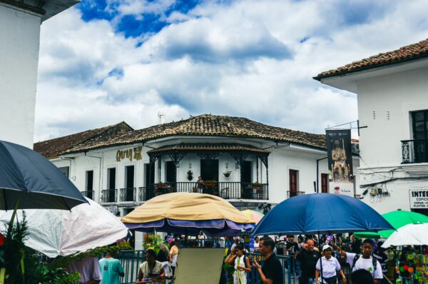 Vibrant market scene in Popayán, Cauca, Colombia, featuring colorful umbrellas and a historic white building under a cloudy sky.