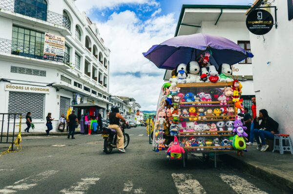 Colorful toy stall under a purple umbrella on a bustling street in Popayán, Cauca, Colombia, with buildings in the background.