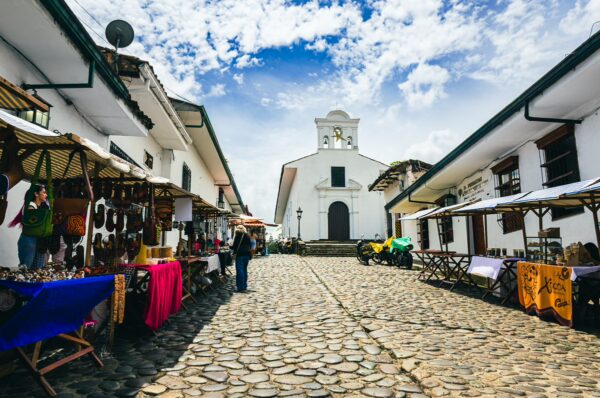 Charming cobblestone street lined with colorful market stalls leading to the white Ermita de Jesús in Popayán, Cauca, Colombia.