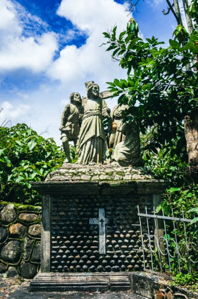 Statue surrounded by lush greenery at Santuario de Belén in Popayán, Cauca, Colombia on a bright day with cloudy skies.