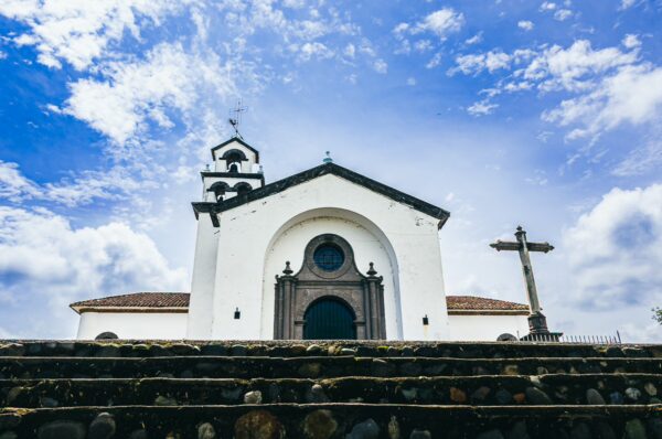 Magnificent white facade of Santuario de Belén rises against a blue sky in Popayán, Cauca, Colombia, framed by stone steps.