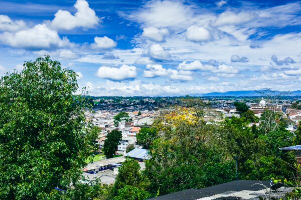Lush greenery frames a panoramic view of Popayán, Colombia, with vibrant colors and dramatic clouds in the sky.