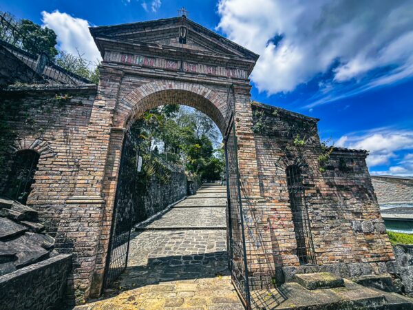 Historic brick archway leading to stone steps at Santuario de Belen, Popayan, Cauca, Colombia under a vibrant blue sky.