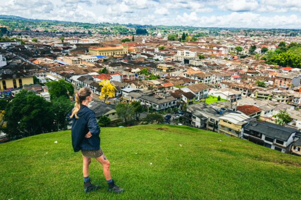 A person stands on a green hill overlooking the colorful rooftops and sprawling landscape of Popayán, Cauca, Colombia.
