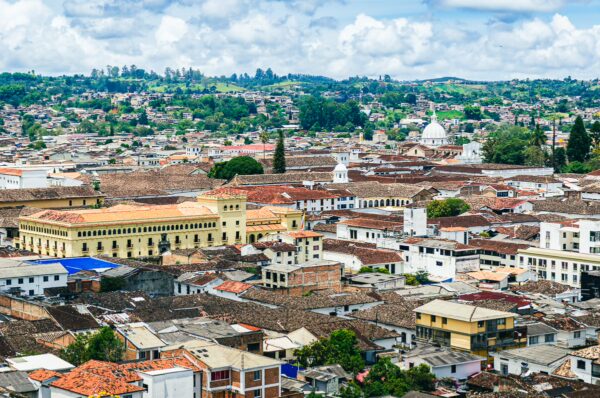 Vibrant rooftops of Popayán, Colombia, with lush hills and notable domes under a bright, cloudy sky.