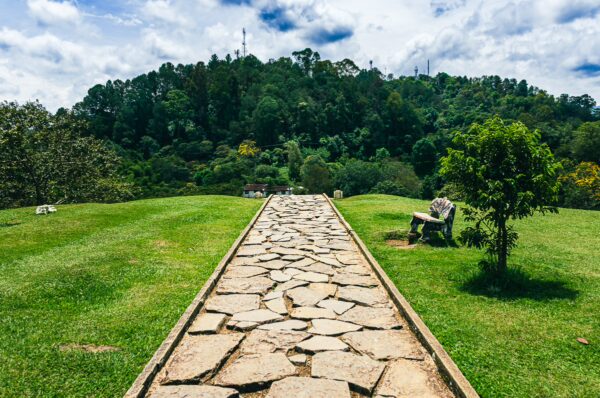 Stone pathway leads through lush green grass towards Morro de Tulcán in Popayán, Cauca, Colombia, under a bright blue sky.