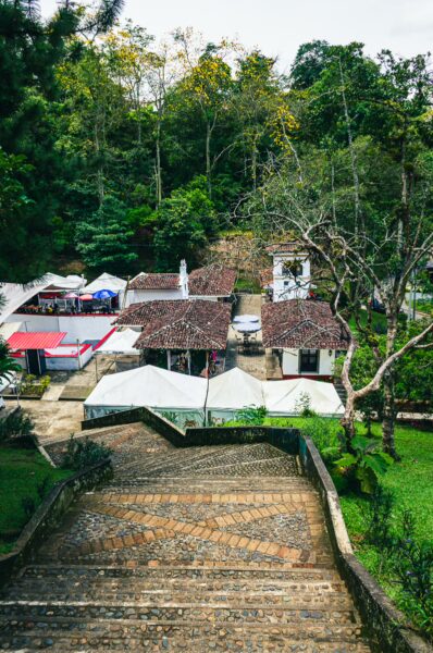 Colorful tents line cobblestone paths leading to charming cottages, framed by lush greenery in Pueblito Patojo, Popayán, Cauca.