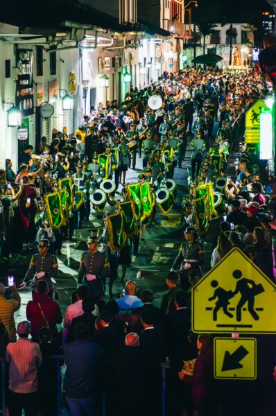Vibrant parade with musicians and dancers filling the streets of Popayán, Cauca, Colombia, surrounded by a festive crowd at night.