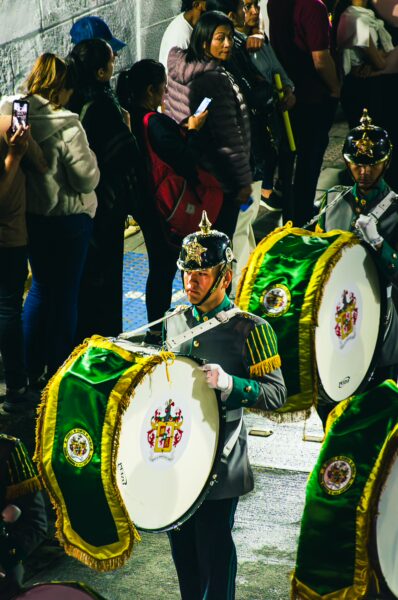 Vibrant drummers in green and gold uniforms perform in Popayán, Colombia, as crowds enjoy the festive atmosphere around them.